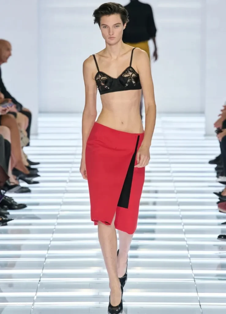 Prada Spring 2027 Look 1 
— red wrap skirt with black vertical panel